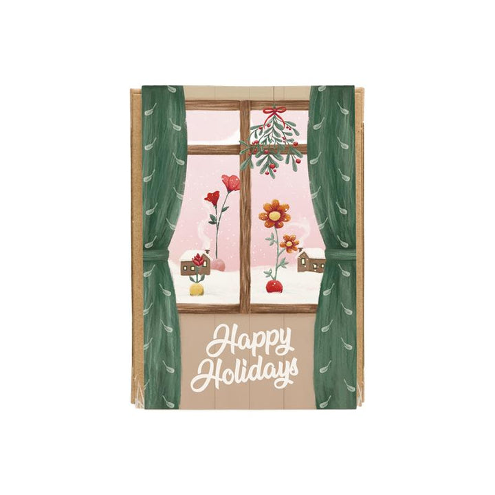 Happy Holidays Gift Box with Window art looking out onto snowy grounds with two balls on top of the snow growing colorful wildflowers and cozy homes in the distance.